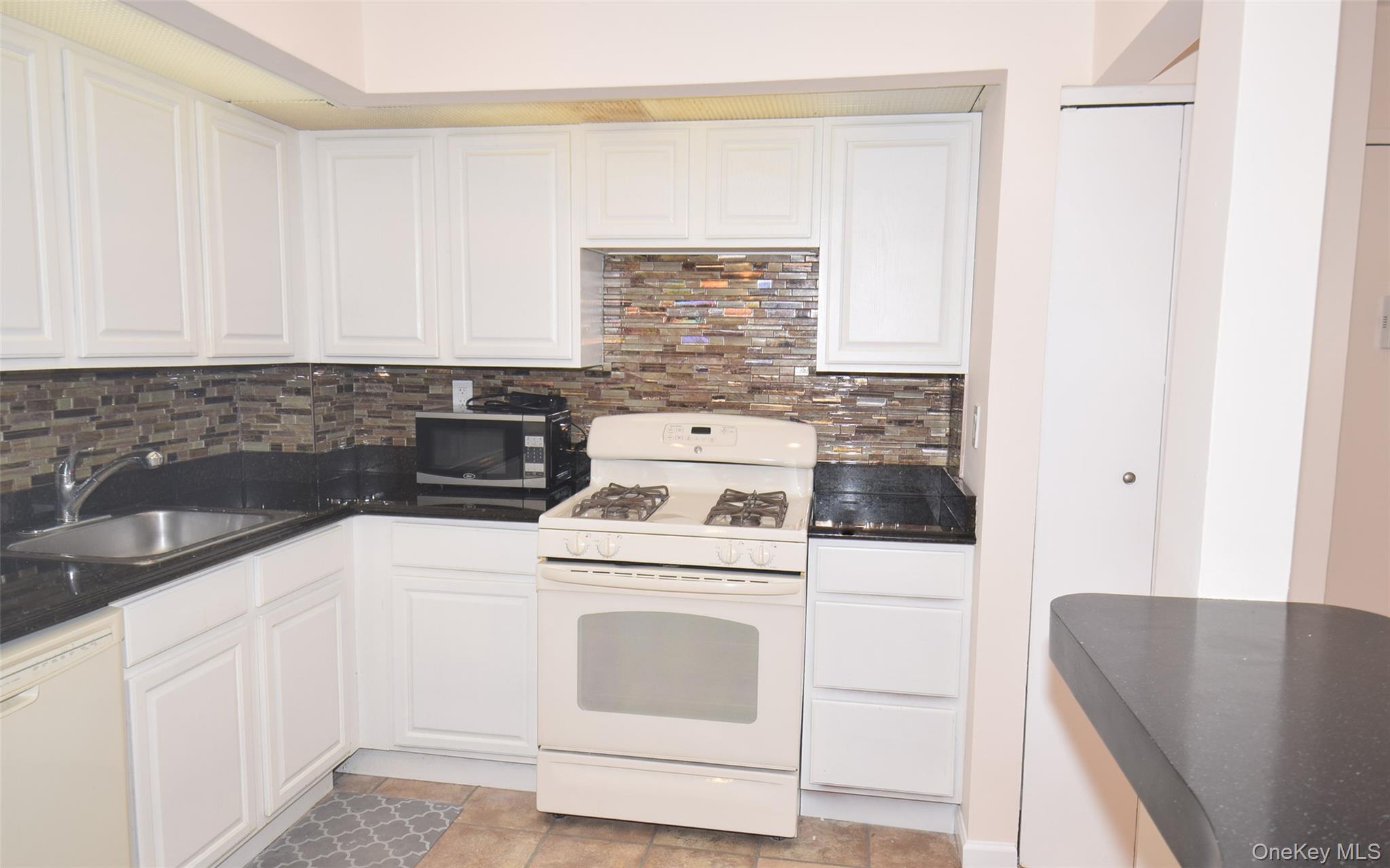 206-14 Emily Road, Unit 42L Queens, NY 11360 - Photo 5 of 14 a kitchen with white cabinets and white appliances