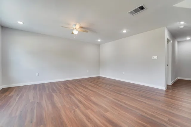 a view of an empty room with wooden floor and a ceiling fan