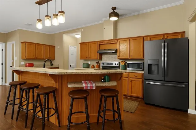a kitchen with stainless steel appliances kitchen island granite countertop a refrigerator a sink dishwasher a stove and a dining table with wooden floor