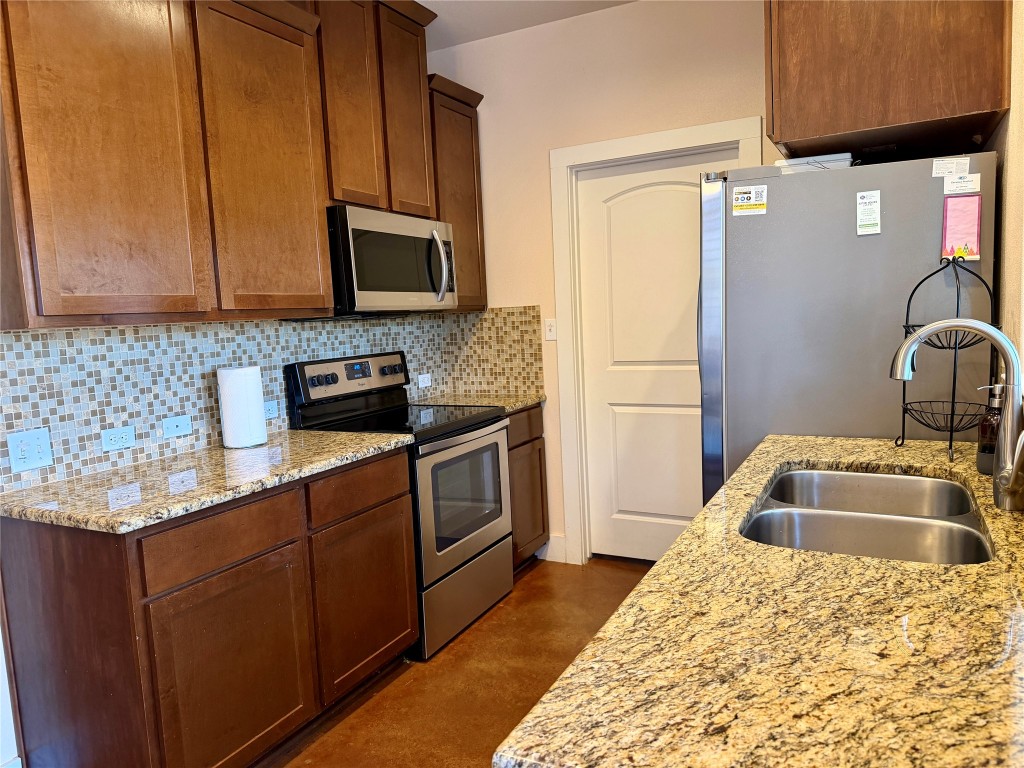 5503 Hiline Road Austin, TX 78734 - Photo 8 of 20 Kitchen featuring appliances with stainless steel finishes, tasteful backsplash, granite countertops, and brown cabinetry