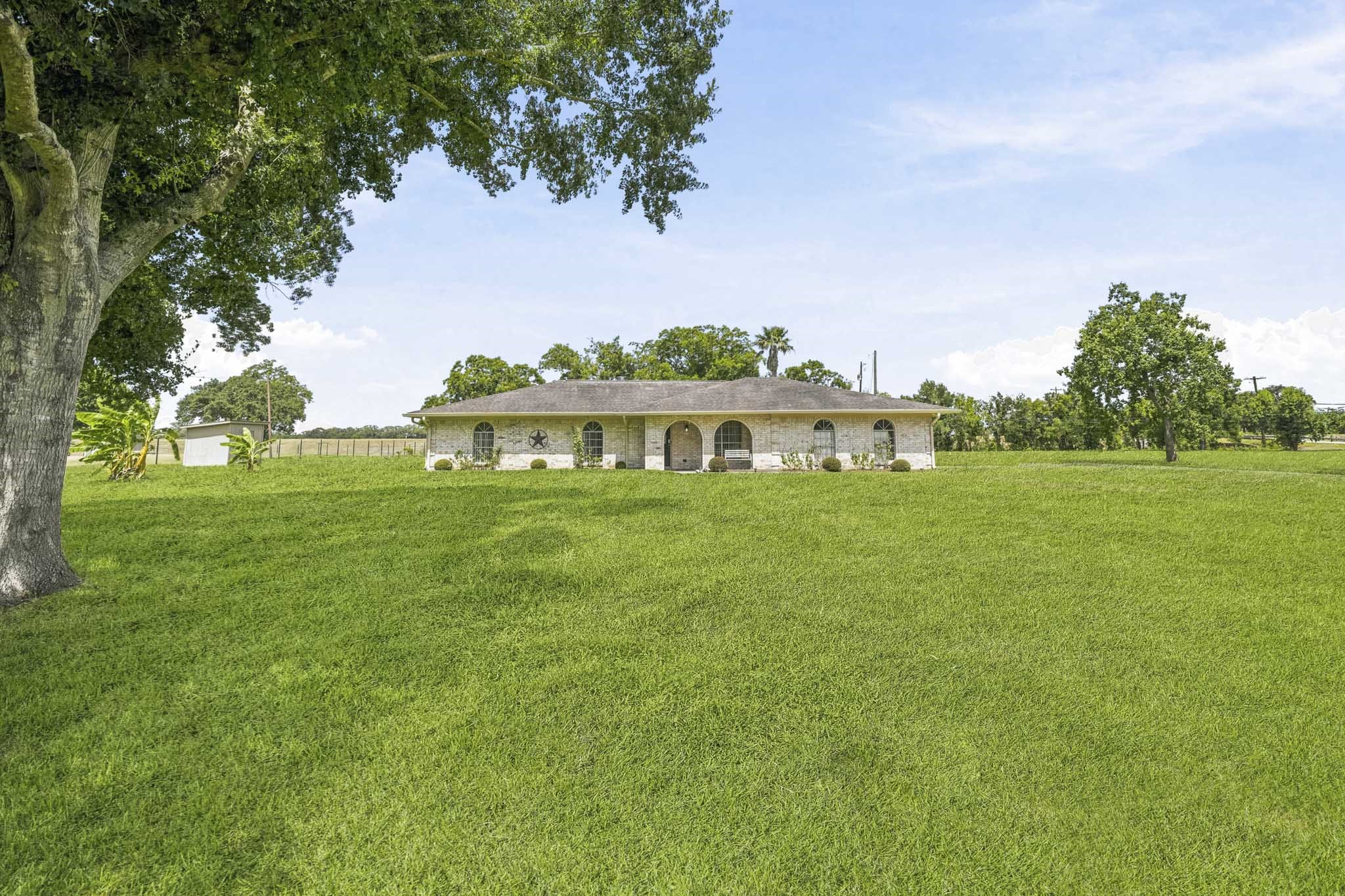 302 Country Road 893 Angleton, TX 77515 - Photo 4 of 26 Charming single-story home set on a spacious, lush green lawn with mature trees. The house features a simple, elegant design with arched windows, providing a serene and private atmosphere. Ideal for those seeking a peaceful rural setting.