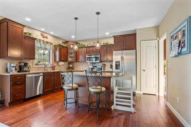 a kitchen with stainless steel appliances granite countertop a refrigerator a stove top oven a sink dishwasher and white cabinets with wooden floor
