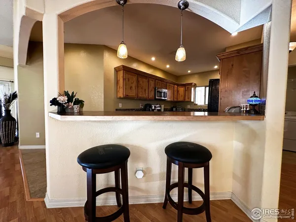 a kitchen with stainless steel appliances granite countertop a sink a stove a refrigerator cabinets and chairs with wooden floor