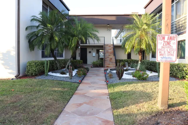 a view of a house with small yard plants and palm trees