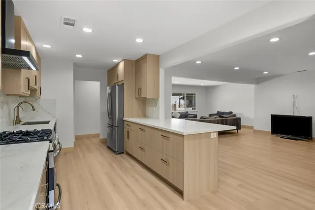 a kitchen with stainless steel appliances a stove a sink a refrigerator and white cabinets with wooden floor