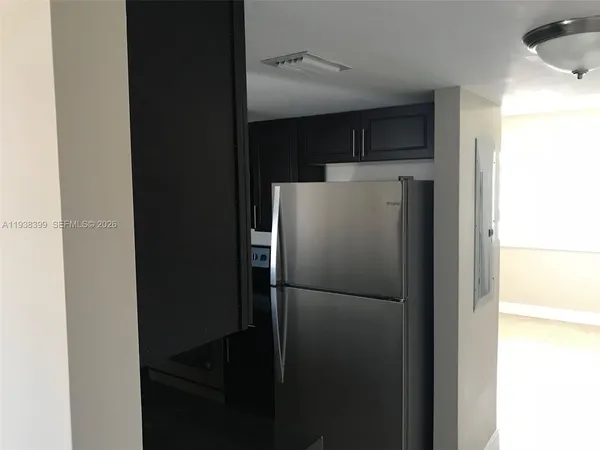 a view of a refrigerator in kitchen and an empty room