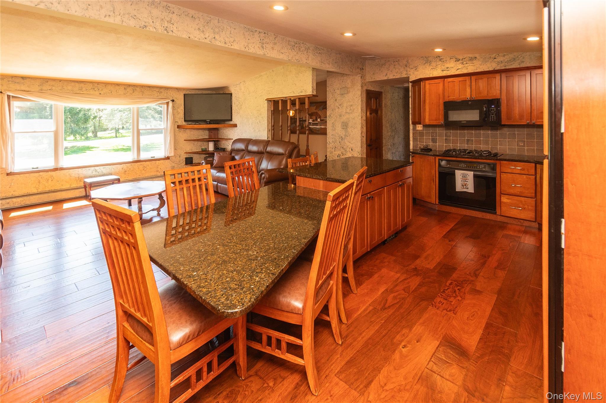 3 Duby Road Wallkill, NY 12589 - Photo 17 of 40 Kitchen and living area featuring wood-finish flooring, a kitchen island with stone countertop, wood cabinetry, a tile backsplash, and a bay window