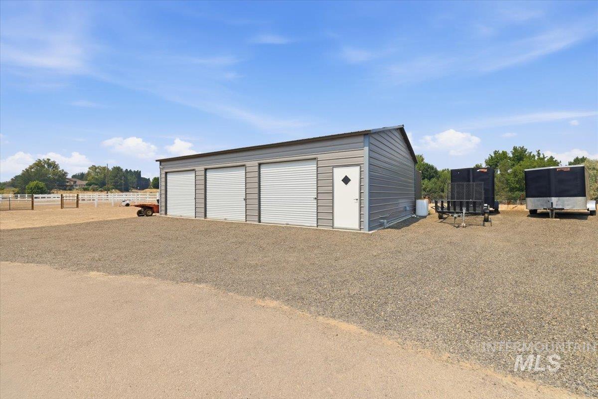 11650 Willis Road Middleton, ID 83644 - Photo 23 of 31 Spacious metal-sided storage building featuring three overhead roll-up doors, gravel apron, and open grounds with fencing and mature trees