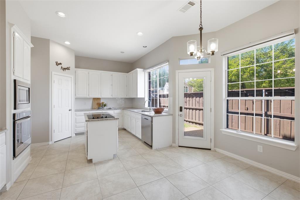 A thoughtfully laid-out kitchen with white raised-panel cabinetry, granite countertops, a center island with cooktop, stainless steel appliances, and an eat-in breakfast area bathed in natural light from a large picture window and a glass back door.