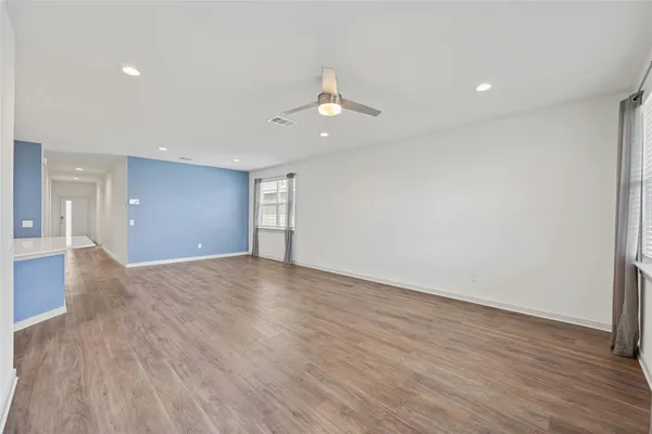 a view of an empty room with wooden floor and a ceiling fan
