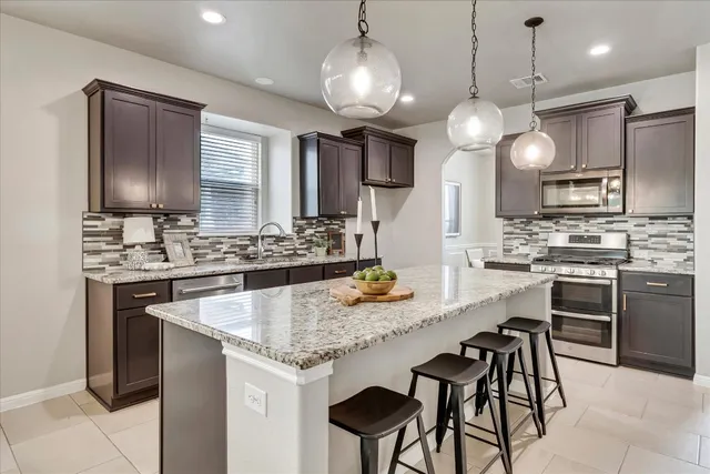a kitchen with stainless steel appliances kitchen island granite countertop a sink a stove a refrigerator and chairs