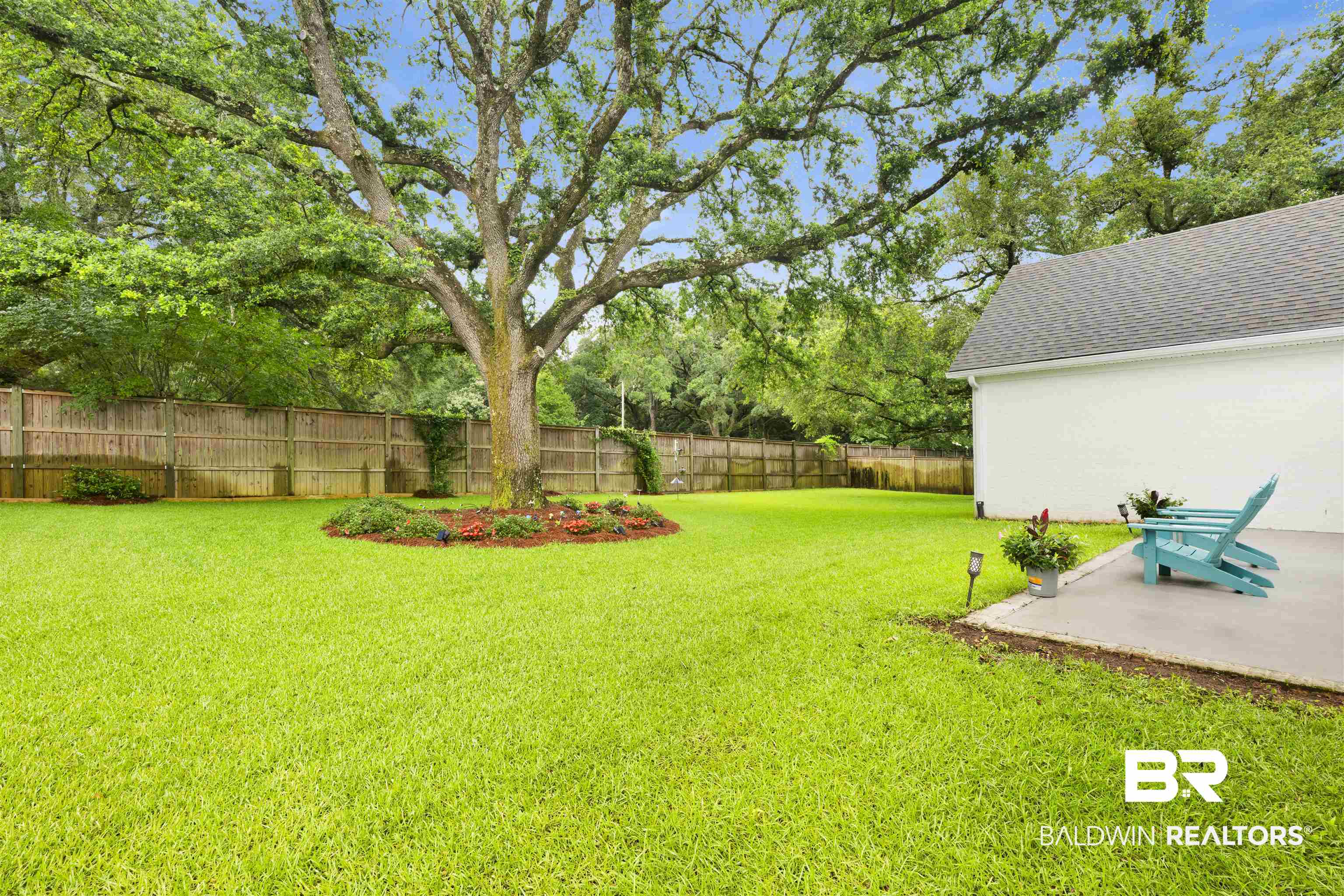 21702 Pillars Street Fairhope, AL 36532 - Photo 37 of 54 Expansive backyard featuring a mature shade tree with a landscaped bed, a large green lawn, a wooden privacy fence, and a concrete patio