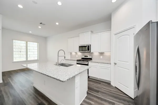 a kitchen with stainless steel appliances granite countertop a refrigerator a stove a sink and white cabinets with wooden floor