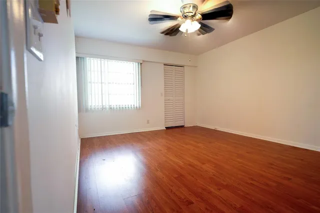an empty room with wooden floor chandelier fan and windows