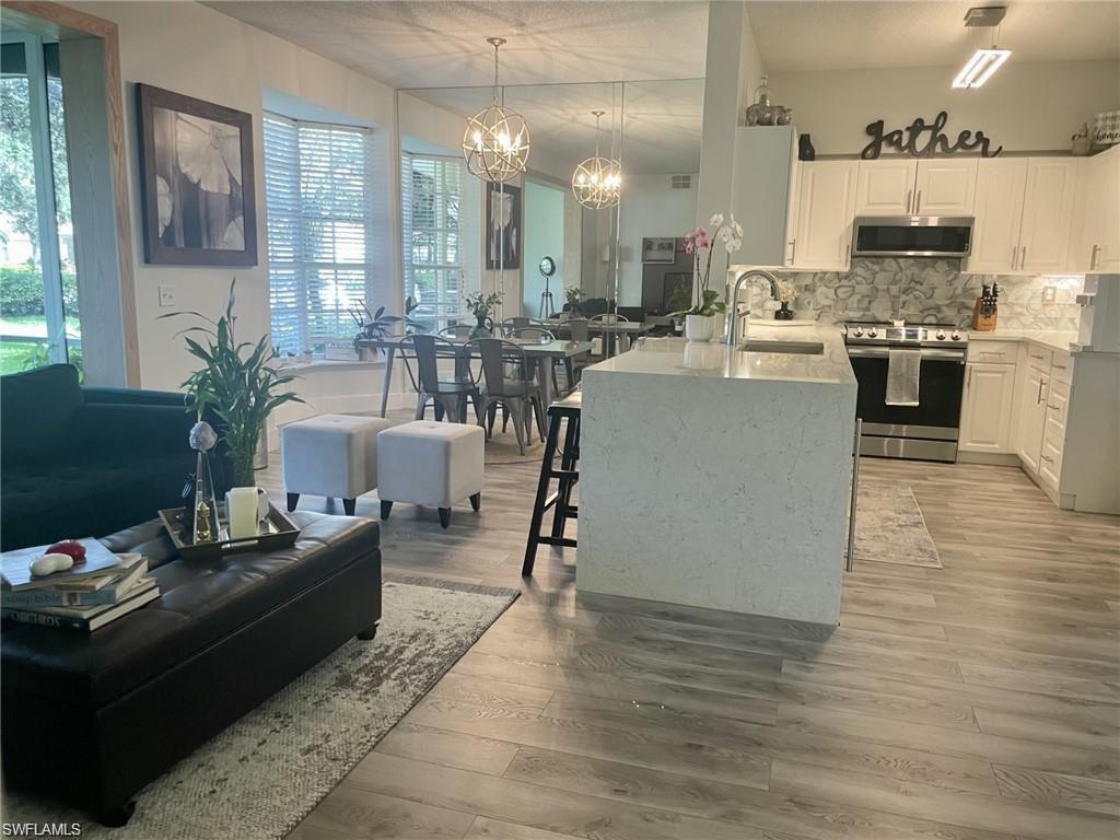 56 Silver Oaks Circle, Unit 102 Naples, FL 34119 - Photo 12 of 12 Kitchen featuring white cabinets, light stone counters, appliances with stainless steel finishes, hanging light fixtures, and decorative backsplash