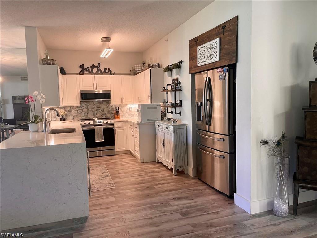 56 Silver Oaks Circle, Unit 102 Naples, FL 34119 - Photo 3 of 12 Kitchen featuring stainless steel appliances, decorative backsplash, light stone countertops, white cabinetry, and light wood finished floors