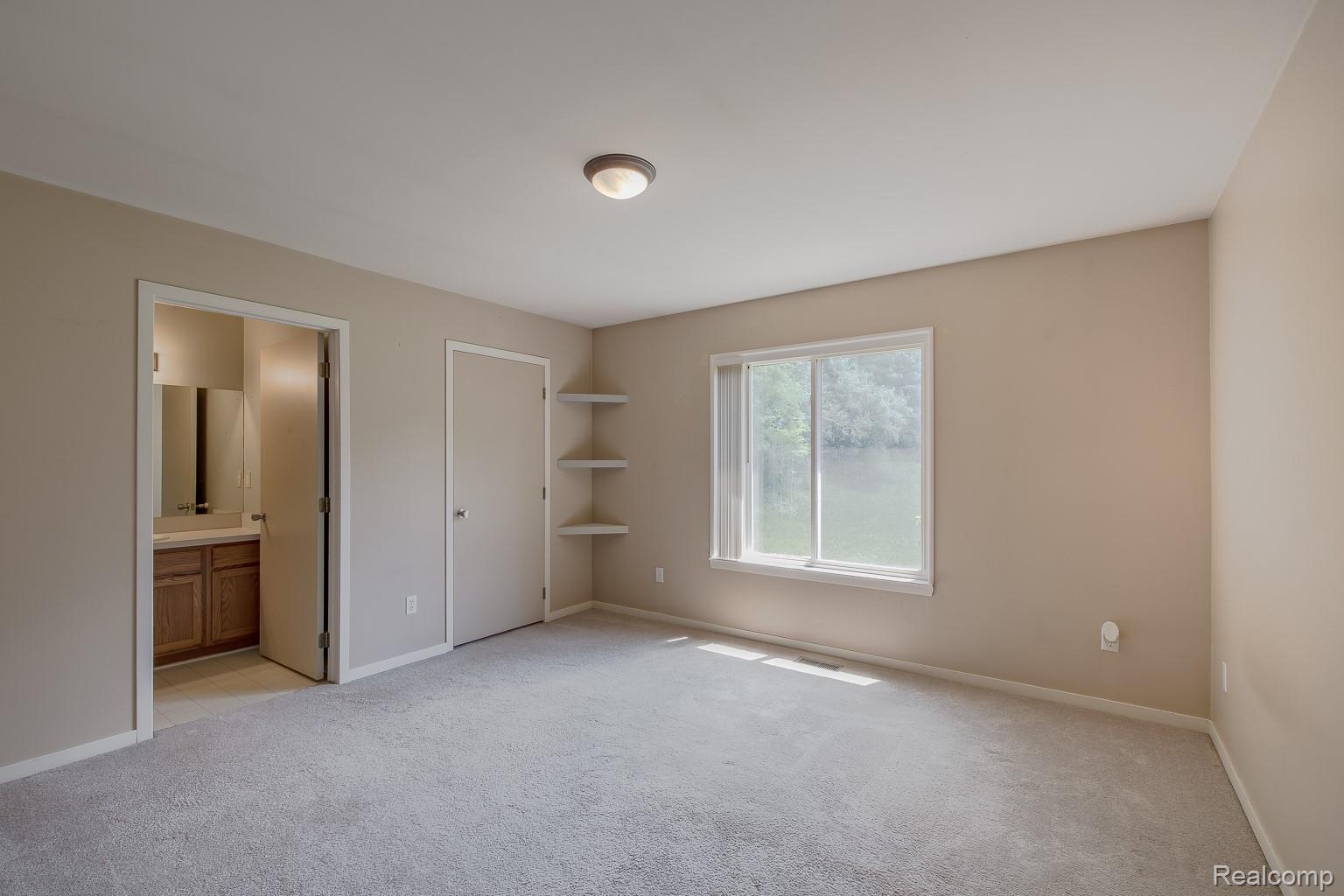 312 Reid Road Highland, MI 48357 - Photo 30 of 47 Carpeted interior space featuring a double-paned window, built-in shelving, a flush-mount ceiling light, and a doorway opening to a vanity with wood cabinetry