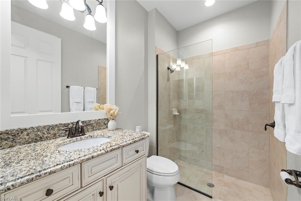 12692 Kinross Lane Naples, FL 34120 - Photo 24 of 47 Guest bathroom with a vanity with a granite countertop, undermount sink, and dark bronze faucet, walk-in shower with tile walls