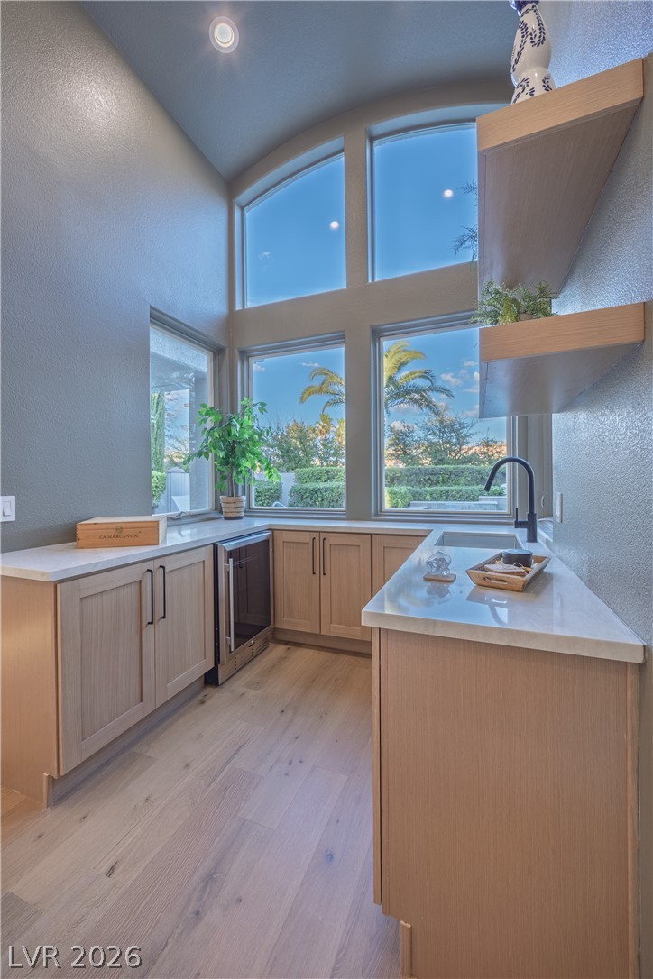 8800 Lusso Las Vegas, NV 89134 - Photo 29 of 85 Kitchen with a textured wall, light wood finish cabinets, light wood-style floors, open shelves, and light stone counters