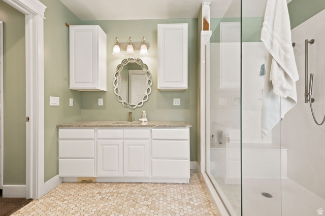 580 North 300 East Logan, UT 84321 - Photo 41 of 74 Bathroom featuring a clear glass shower enclosure with a built-in bench, hexagon tile flooring, a single vanity with stone-finish countertop, white cabinetry, and a decorative wall mirror