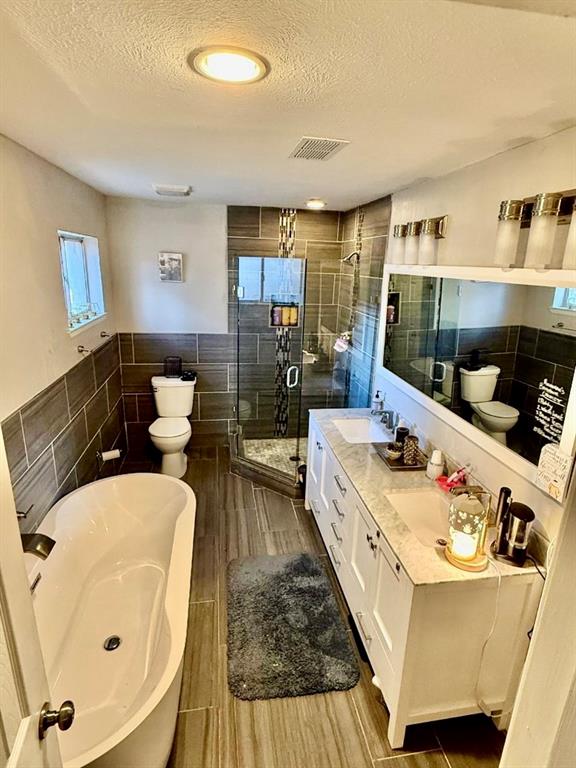 2888 Reedcroft Drive Farmers Branch, TX 75234 - Photo 11 of 32 Primary Bathroom with tile walls, a freestanding bath, double vanity, a textured ceiling, and a separate shower