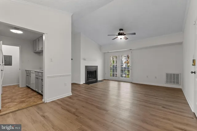 a view of an empty room with wooden floor and a ceiling fan
