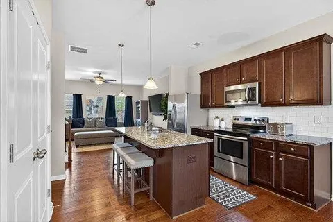 a kitchen with stainless steel appliances granite countertop a stove a sink dishwasher a microwave oven and a dining table with wooden floor