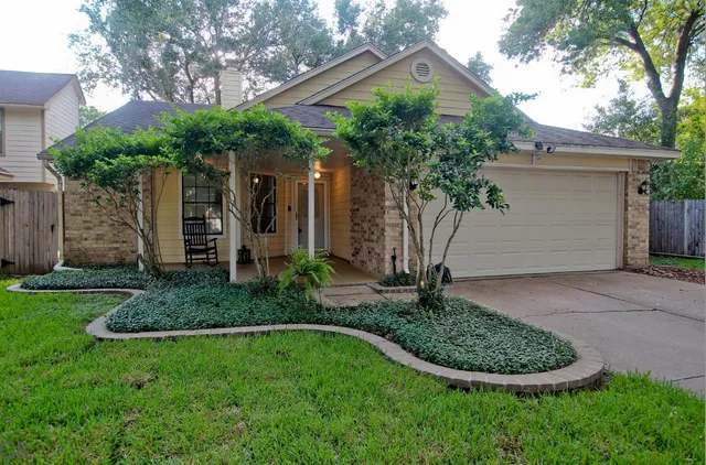 a view of a house with a yard plants and a large tree