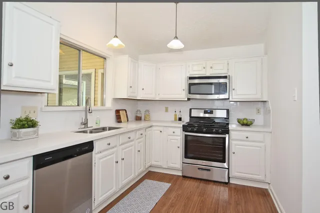 a kitchen with stainless steel appliances white cabinets a sink a stove a microwave and wooden floors