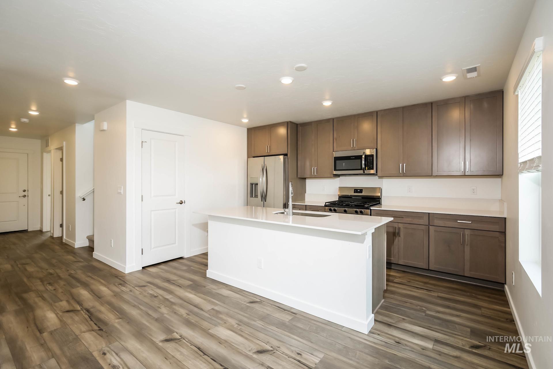 Kitchen featuring gray cabinetry, stainless steel appliances, a center island, and wood-finish flooring