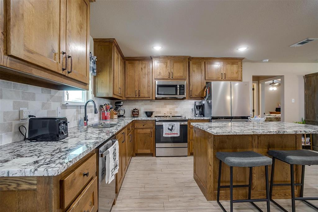 2140 Brown Loop Poolville, TX 76487 - Photo 9 of 38 a kitchen with stainless steel appliances granite countertop a stove top oven a sink dishwasher a dining table and chairs with wooden floor