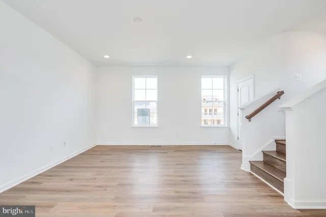 a view of an empty room with wooden floor and a kitchen