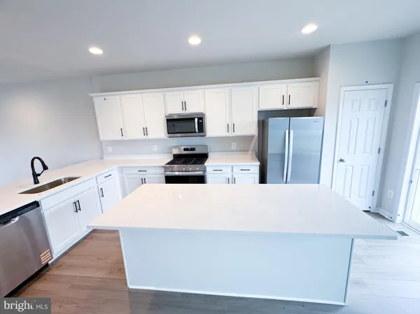 a large white kitchen with stainless steel appliances a refrigerator a sink a microwave a refrigerator and white cabinets