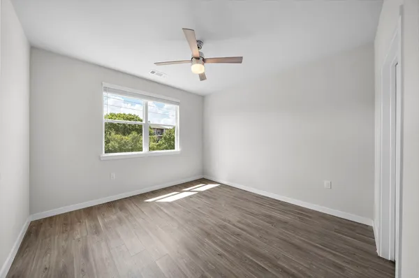 an empty room with wooden floor a ceiling fan and windows