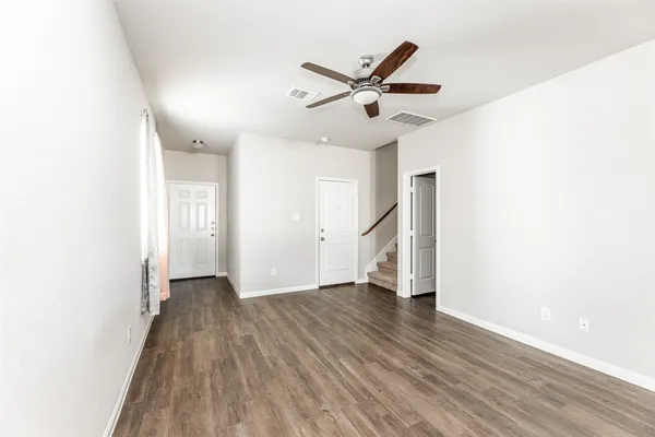 a view of an empty room with wooden floor and a ceiling fan