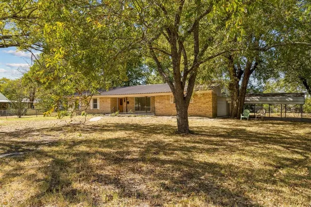 a backyard of a house with large trees and table and chairs