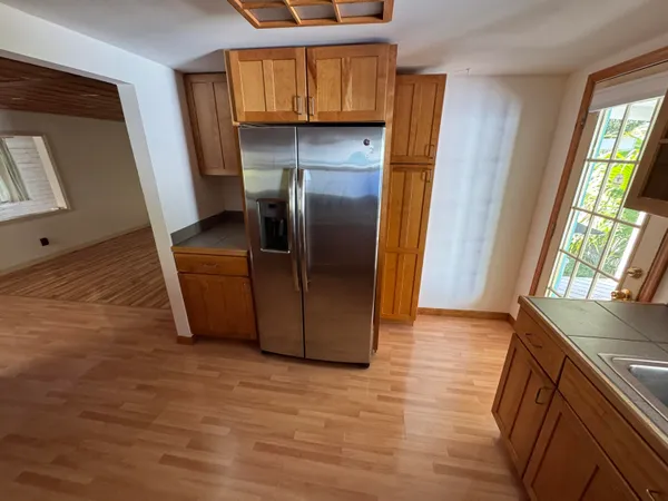 a view of a refrigerator in kitchen and an empty room in wooden floor