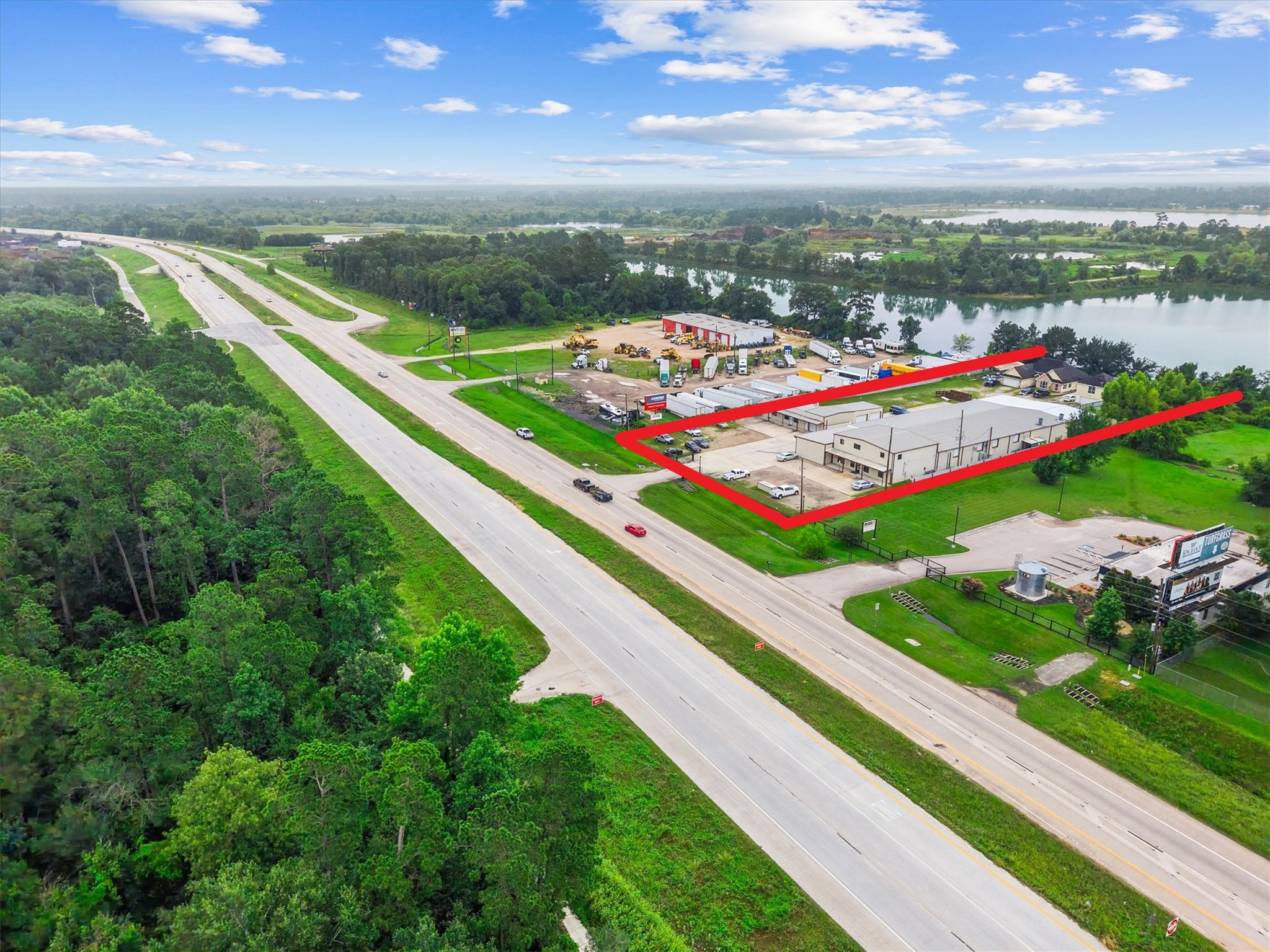 11066 Sh 242 Conroe, TX 77385 - Photo 2 of 21 This aerial photo showcases a commercial property outlined in red, located next to a highway with ample parking space. The area features lush greenery and a nearby body of water, offering a mix of accessibility and natural beauty.