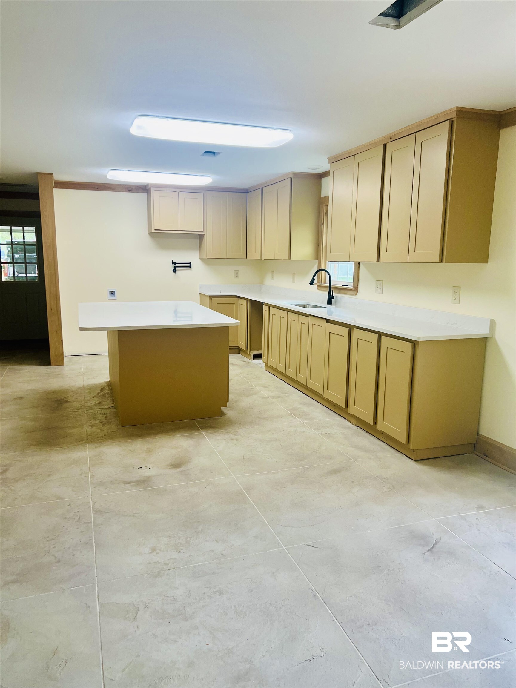 29685 Gardner Road Elberta, AL 36530 - Photo 5 of 16 Kitchen featuring a central island with a solid surface countertop, perimeter cabinetry with wood trim, a single basin sink with a gooseneck faucet, and light-toned floor tiling