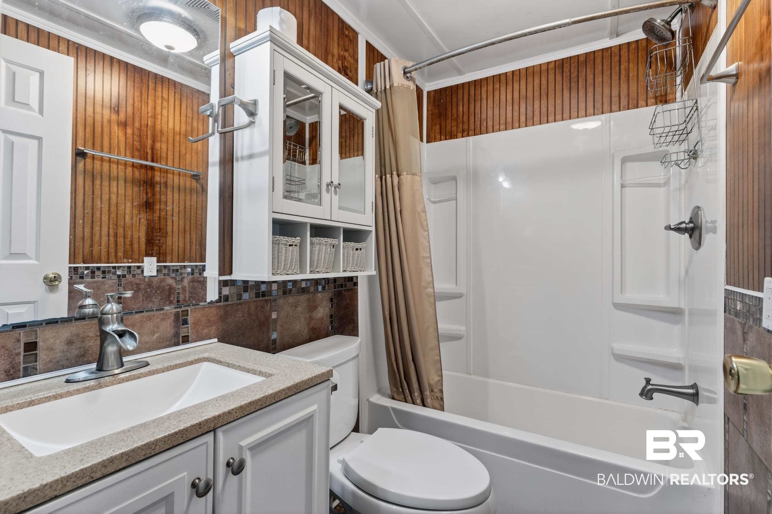 24903 Patterson Road Robertsdale, AL 36567 - Photo 50 of 57 Bathroom featuring wood-finish paneling, a full bathtub with shower, a vanity with a rectangular sink and stone-look countertop, and a built-in wall cabinet with glass doors