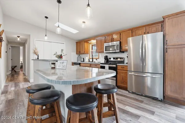 a kitchen with stainless steel appliances granite countertop a refrigerator a oven a stove a sink a dining table and chairs with wooden floor