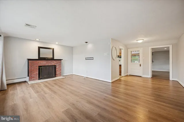 a view of an empty room with wooden floor fireplace and a window