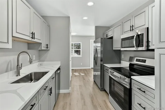 a kitchen with stainless steel appliances granite countertop a sink dishwasher a stove top oven a refrigerator with white cabinets and wooden floor