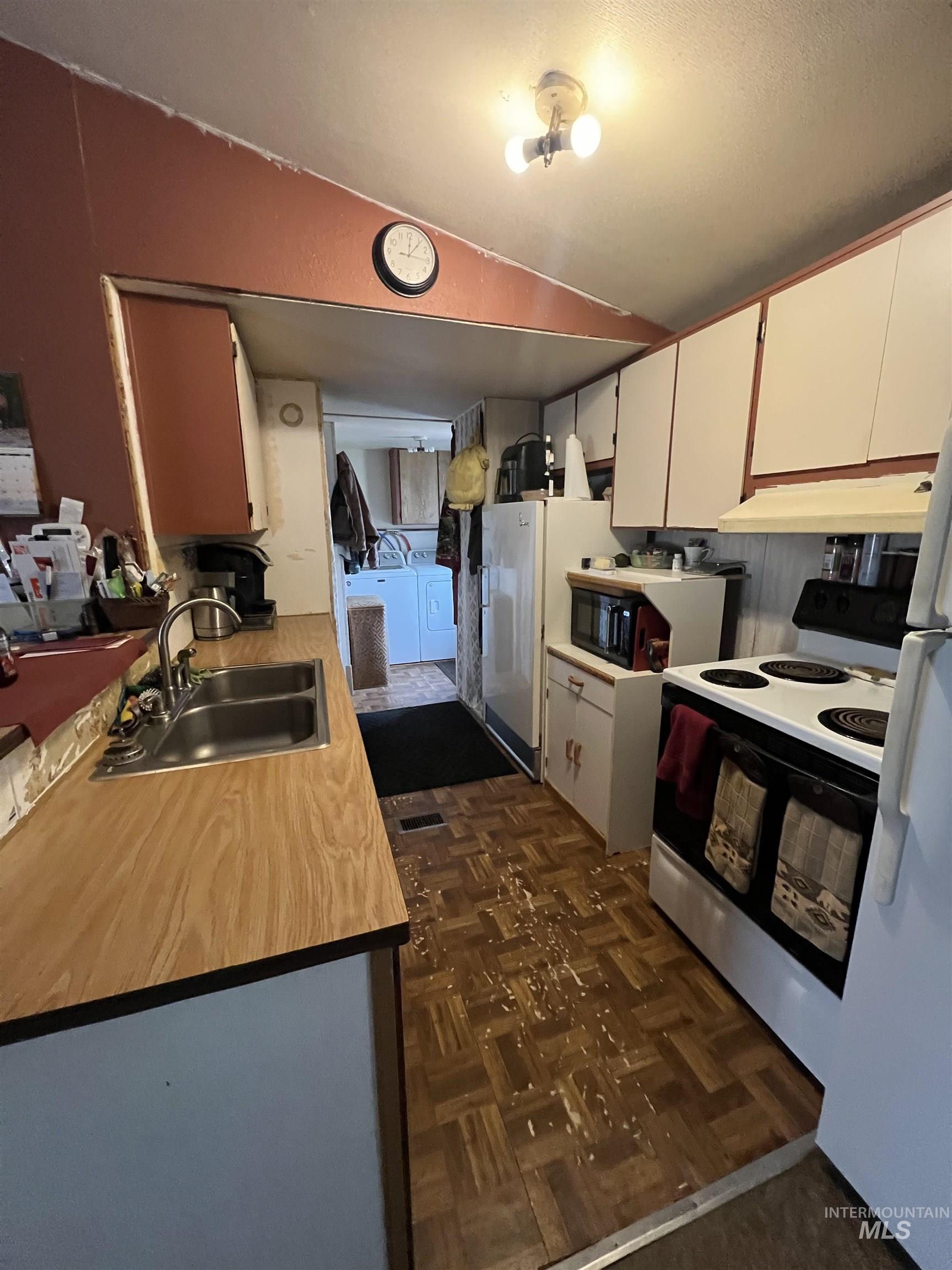 23743 Stephen Lane Parma, ID 83660 - Photo 32 of 34 Kitchen with white appliances, light countertops, washing machine and dryer, white cabinets, and parquet floors