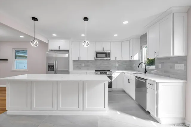 a kitchen with stainless steel appliances kitchen island a sink a stove a refrigerator and white cabinets