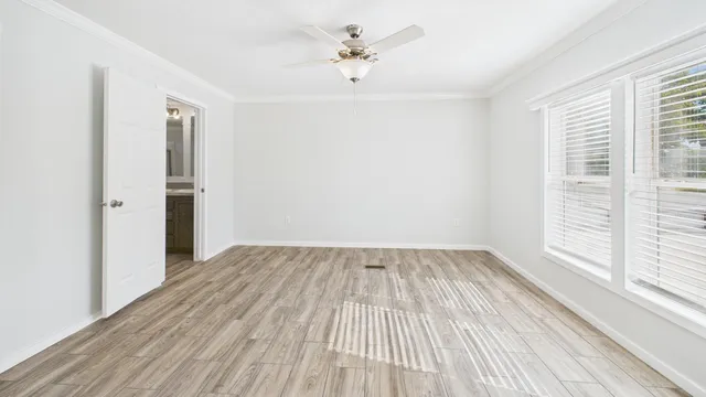 an empty room with wooden floor ceiling fan and windows