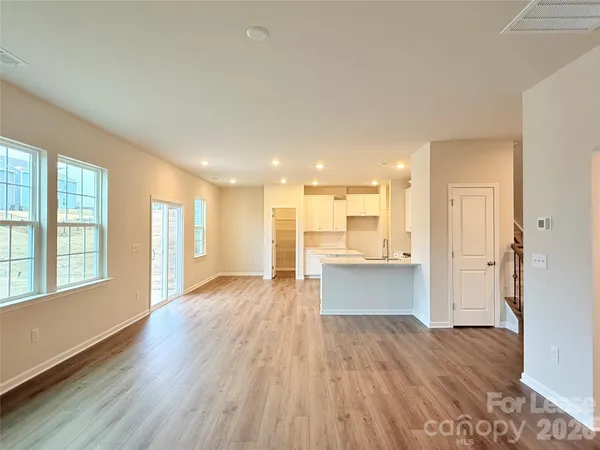 a view of an empty room and kitchen with wooden floor and a window