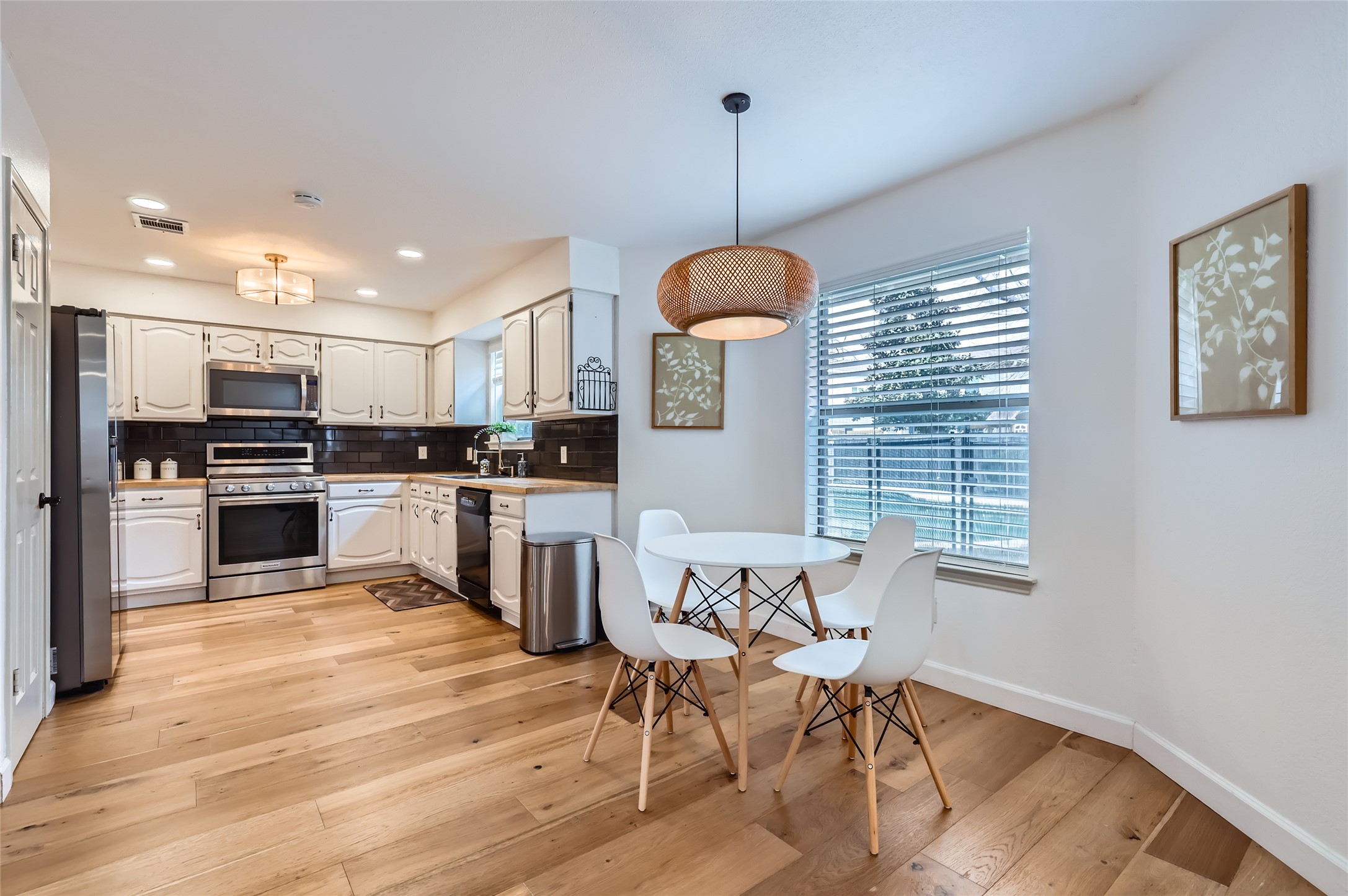 13205 Kepler Cove Austin, TX 78729 - Photo 11 of 34 Kitchen with wood-finish flooring, white cabinetry with dark hardware, stainless steel appliances, and dark subway tile backsplash