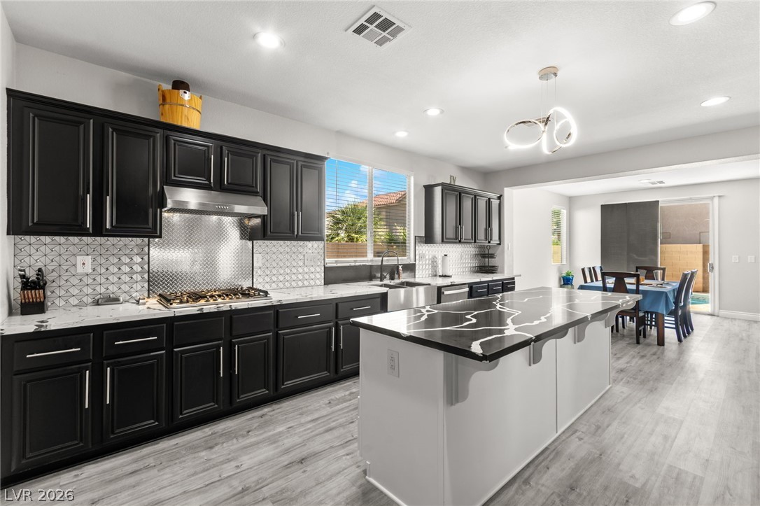 5601 Rocky Ravine Avenue Las Vegas, NV 89131 - Photo 24 of 71 Kitchen with dark cabinets, light wood-type flooring, a kitchen island, and dark stone counters
