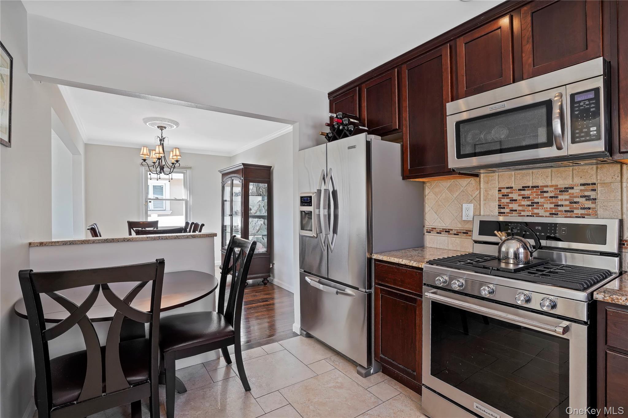 91-03 156th Avenue Queens, NY 11414 - Photo 12 of 50 Kitchen featuring appliances with stainless steel finishes, dark brown cabinetry, ornamental molding, light stone countertops, and a chandelier